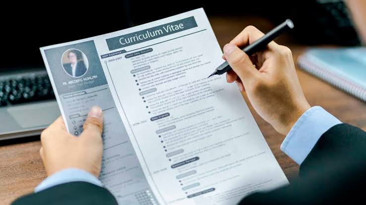 Pessoa revisando um currículo com caneta na mão